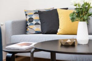 Sofa mit Zierkissen, im Vordergrund 2 Clubtische mit frischen Blumen